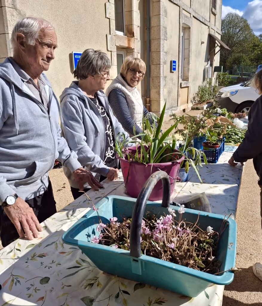 Trois bénévoles derrière la table du troc, devant un panier de cyclamens et un pot de plantes vertes