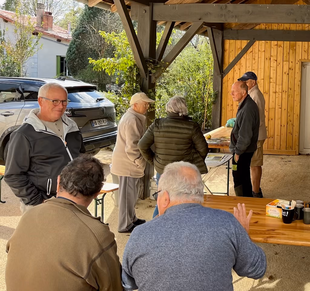 Les visiteurs échangent sous le préau en bois, autour des tables